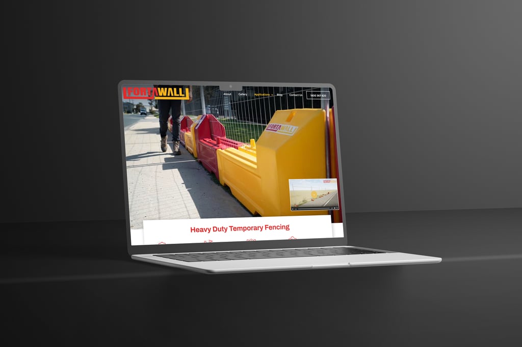 A laptop displays a website featuring heavy-duty temporary fencing with an image of yellow and red barriers along a pavement. The background is a plain, dark surface.