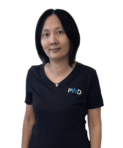 A woman with straight, shoulder-length black hair stands against a plain white background. She is wearing a black T-shirt with the letters PWD in blue and white on the left side of her chest.