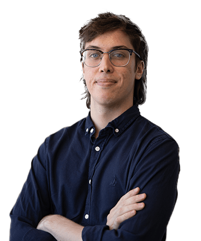 Harrison Sharrett, a young adult with glasses and brown hair, stands with arms folded in a dark blue button-up shirt, looking confidently at the camera against a plain white background.