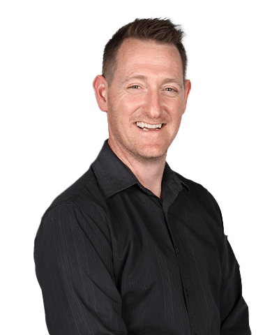 Chris Merton, a man with short light brown hair and fair skin, smiles whilst wearing a black button-up shirt. He is standing against a plain white background.