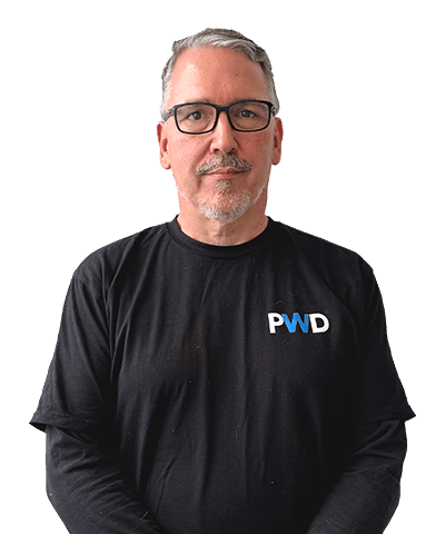 A middle-aged man with short grey hair, glasses, and a goatee wears a black long-sleeve shirt with PWD written on it. Mike Zittritsch stands against a plain white background.