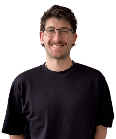 A smiling man with short brown hair, glasses, and a moustache is wearing a black T-shirt and standing against a plain white background.
