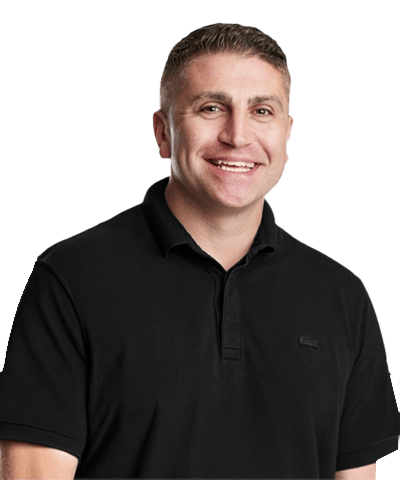 A man with short light brown hair, wearing a black collared shirt, is smiling and posing against a plain white background.