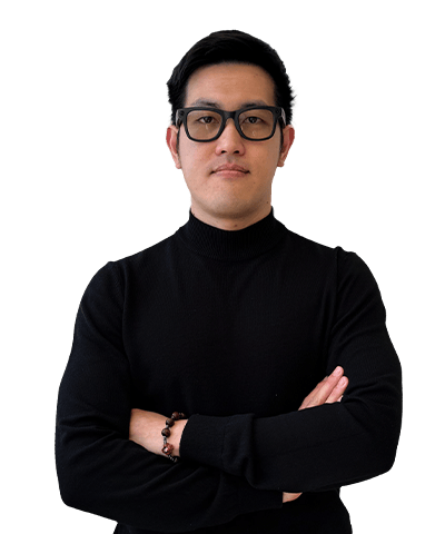 A person wearing black glasses and a black polo-neck jumper stands with arms crossed, looking confidently at the camera against a plain white background.