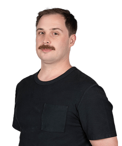 Warrun Lewis, a man with short brown hair and a moustache, is wearing a black T-shirt. He stands against a plain white background, looking slightly to the side with a neutral expression.