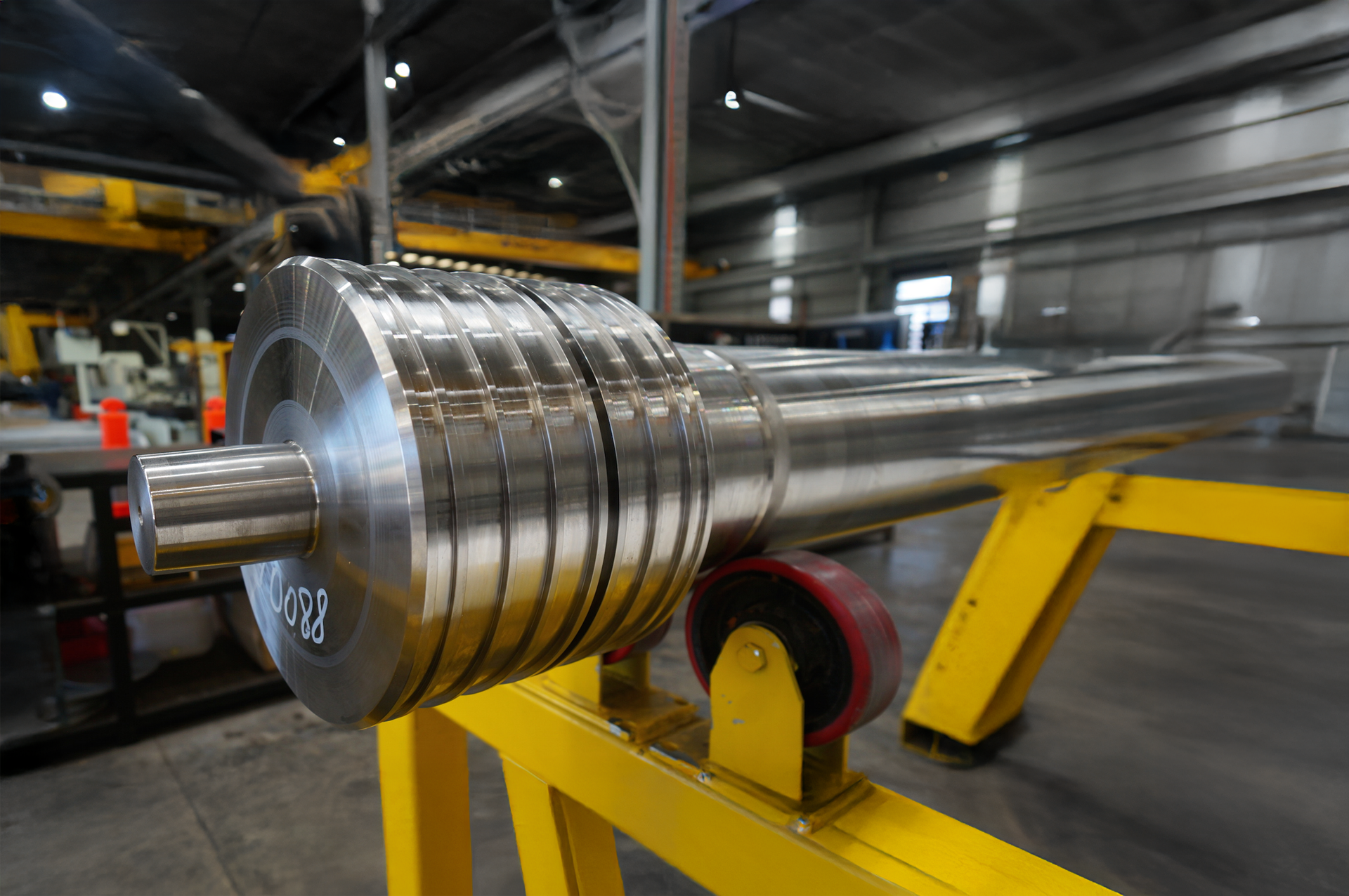 A large, polished metal industrial cylinder with grooves is mounted on yellow supports inside a spacious, well-lit factory, showcasing the precision of Maskills Mechanical Services.