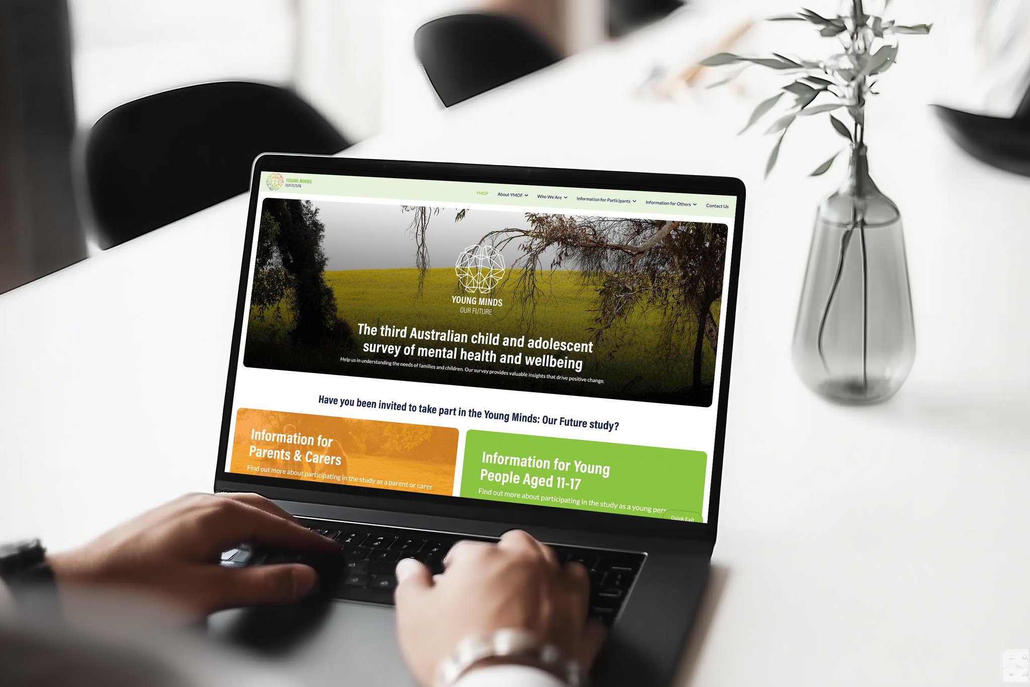 A person types on a laptop displaying a website titled “Young Minds Matter,” with sections for parents, carers, and young people about a mental health and wellbeing survey shaping the future in Australia.