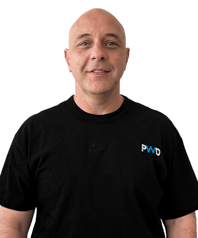 A smiling bald man, Raf Baldasso, wearing a black Nike t-shirt with a small “PWD” logo on the left side stands against a plain white background.