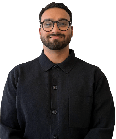 A man with short dark hair, a beard, and glasses is smiling slightly. He is wearing a dark button-up shirt with a collar and is standing against a plain white background.