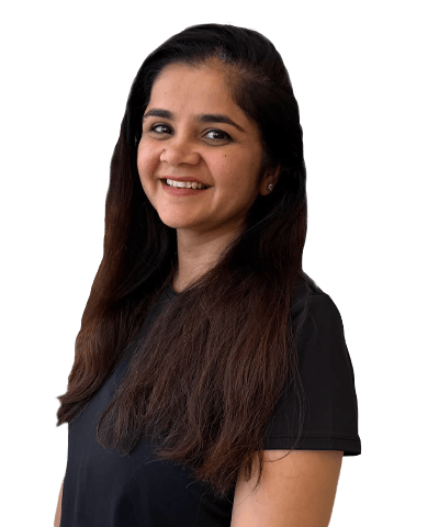 Aastha Chopra, a woman with long dark hair, wearing a short-sleeved black top, smiles whilst looking slightly to the side against a plain white background.