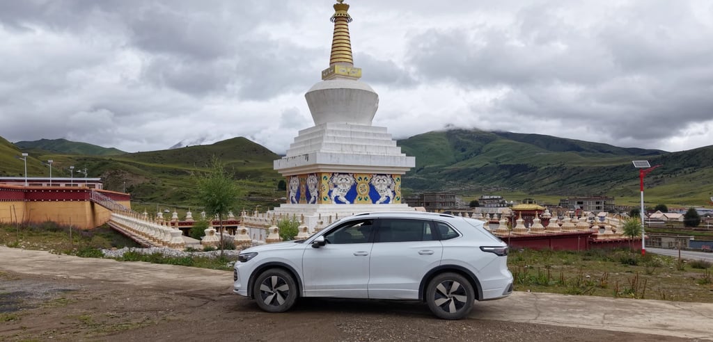 A white SUV parked by a Tibetan stupa, green hills behind