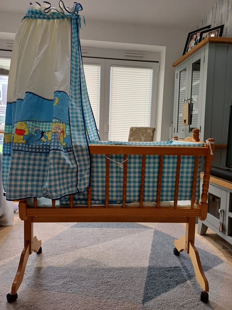 Swinging crib complete with winnie the pooh design bumper, drapes, quilt cover and bottom sheet.