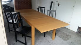 extending light brown wood dining table with 4 blacks chairs