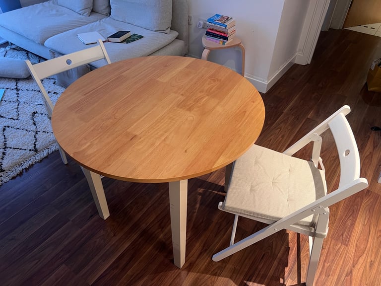 Round Wooden Dining Table with Two White Folding Chairs