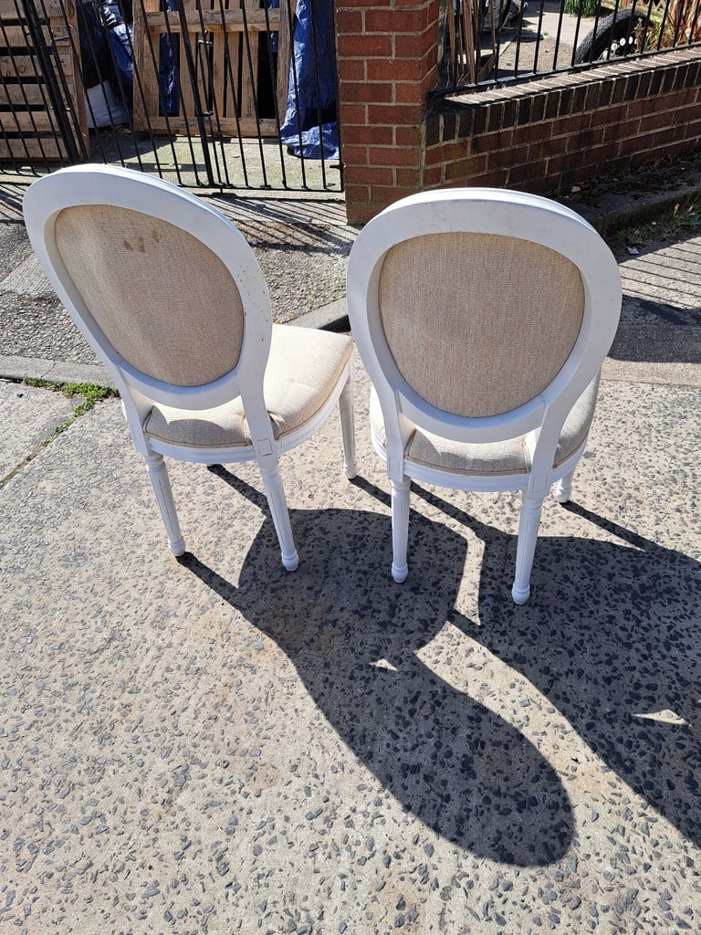 2 white wood framed chairs with cream padded seats and backs