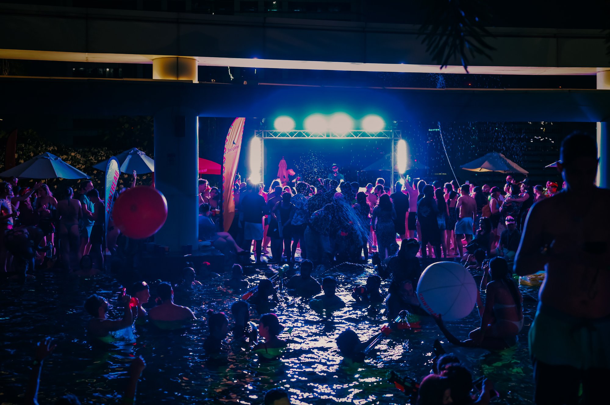 Night-time rooftop pool party in full swing at Centara Grand, CentralWorld, with the DJ stage lit up over the pool