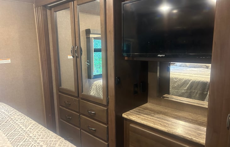 The bedroom area has a closet, 6 drawers for clothes, a tv, with a counter under and with three more drawers, a nightstand on each side of the bed, and cabinets above the bed.