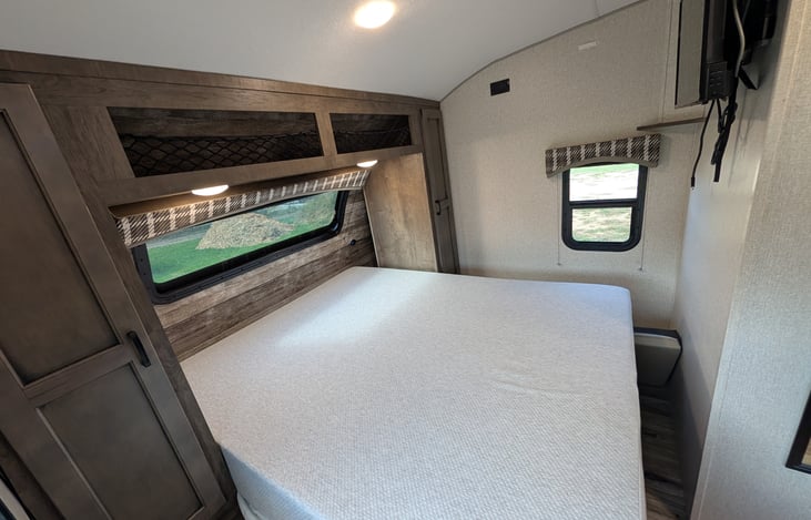 Cozy front bedroom featuring an upgraded residential mattress for a great night's sleep, TV, and bright windows with a massive automotive panoramic front view!