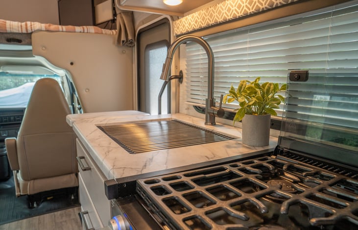 3 burner stove with oven and large single basin sink with dish drying rack.