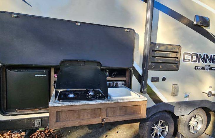 Outdoor kitchen includes small bar sized fridge, 2 burner propane stove and sink.