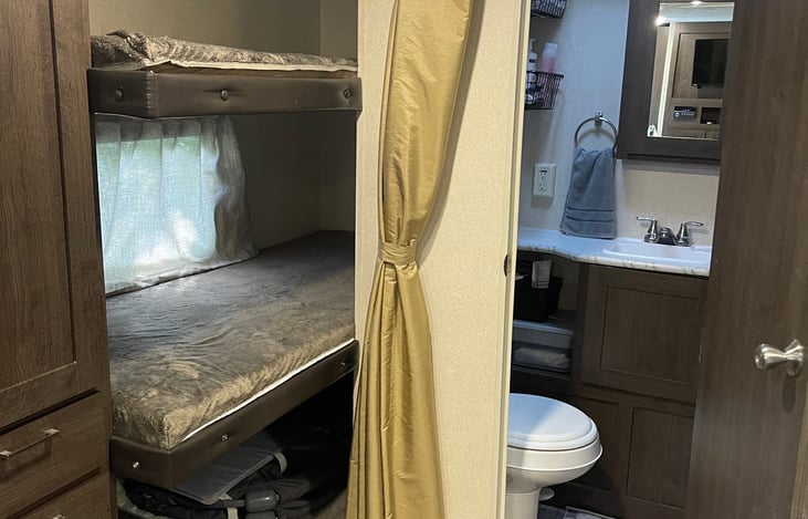 Triple bunks, closet and drawers to the left and bathroom to the right.