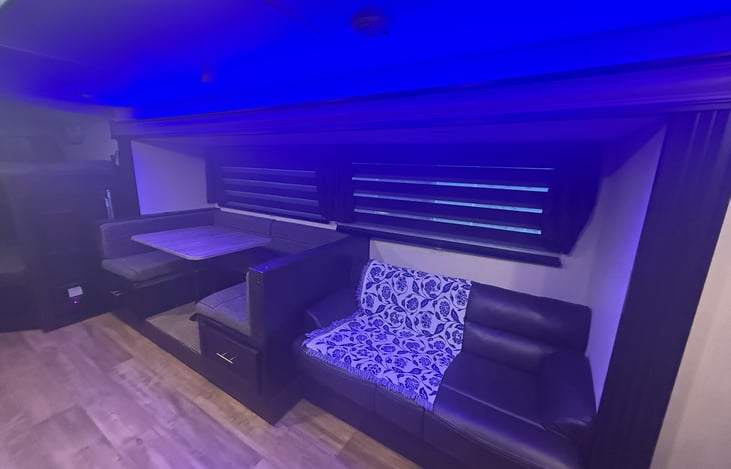 Living room with blue and yellow lighting showing dinette and jackknife couch.