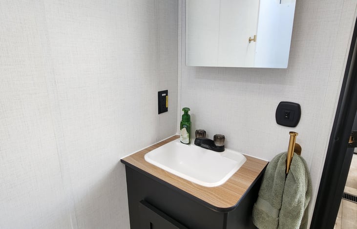 Bathroom area. Extra toilet paper, hand towel, and shower towels underneath. Mirror opens up as a medicine cabinet.