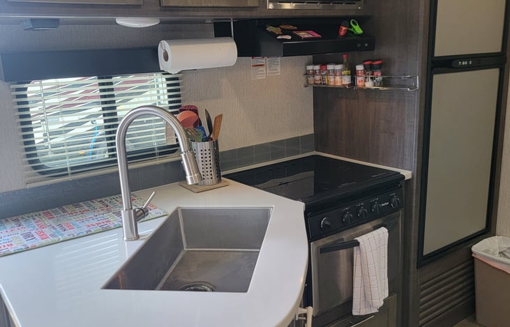 Kitchen with 3-burner stove, oven, microwave, and refrigerator. Stocked with pots, pans, plates, cups, and silverware.