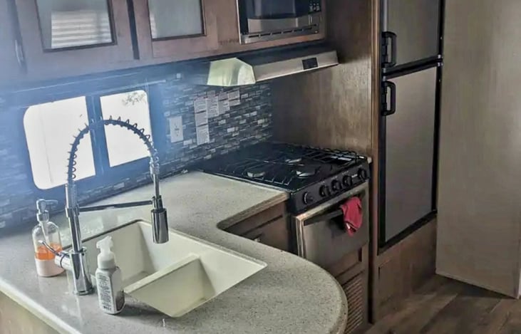 Spacious Kitchen with microwave, Gas stove, oven, Freezer with ice cube tray, and Refrigerator stocked with complimentary bottled water.