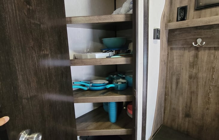 Pantry fully stocked with bowls, plates, cutlery, trash bin, cooking utensils