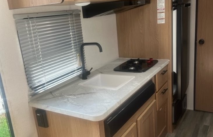 Two burner stove with a microwave above, large fridge.