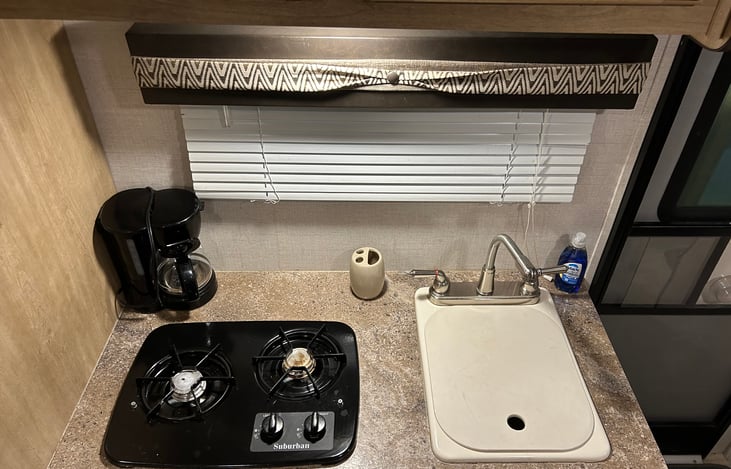 Sink, gas cooktop, and included coffee maker. Under sink storage includes: plastic baggies, trash bags, laundry drying line and pins, toilet paper, disinfectant wipes, and paper towels.