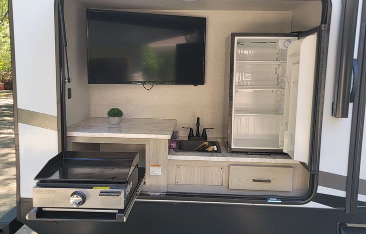 Outside entertainment center with grill and large refrigerator and sink.