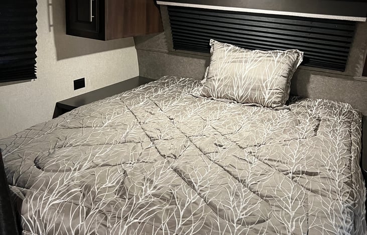 RV queen bed with storage on either side of the bed, as well as a shelf above the bed.