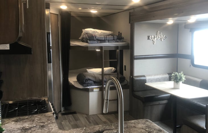 View from the entrance door looking across the sink into the living space.  Double sized bunk beds straight forward, horseshoe dinette to the right