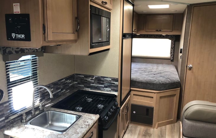 Kitchen area with gas stove, sink, microwave and rear bed.