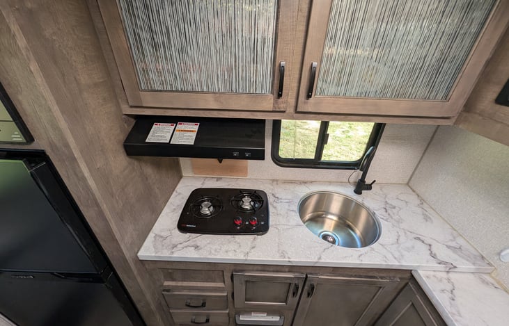 Spacious rear kitchen layout with ample counter space, double-door fridge, stove, microwave & deep sink. Perfect for prepping campsite meals with all the comforts of home!