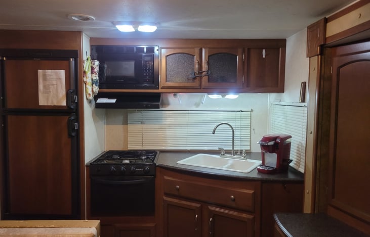 Kitchen. Showes microwave, 3 burner stove & oven, refrigerator, Kurig & large cupboard to the left.