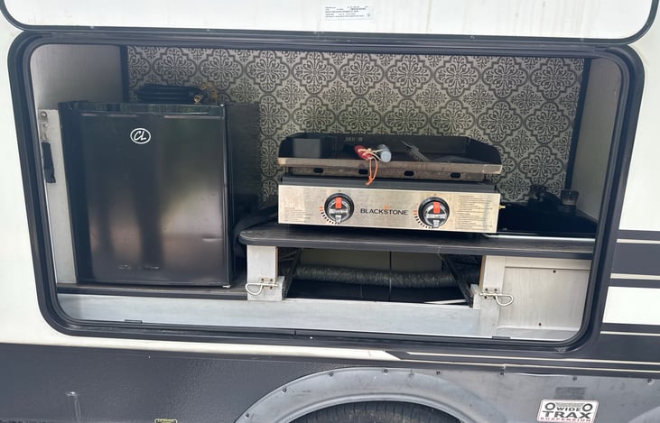 Outdoor kitchen with refrigerator, black stone and sink.