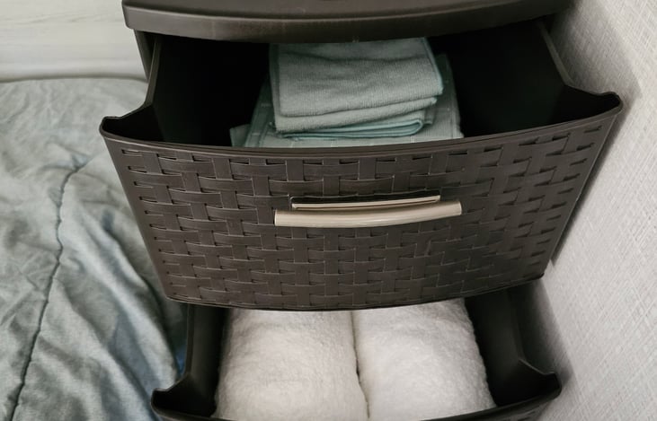 Small three drawer plastic shelf with four bath towels, four dish towels and four wash cloths.