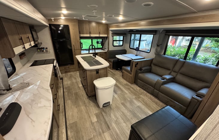 Open and spacious living area with kitchen island, theater seating, and large windows that make the RV feel bright and comfortable.