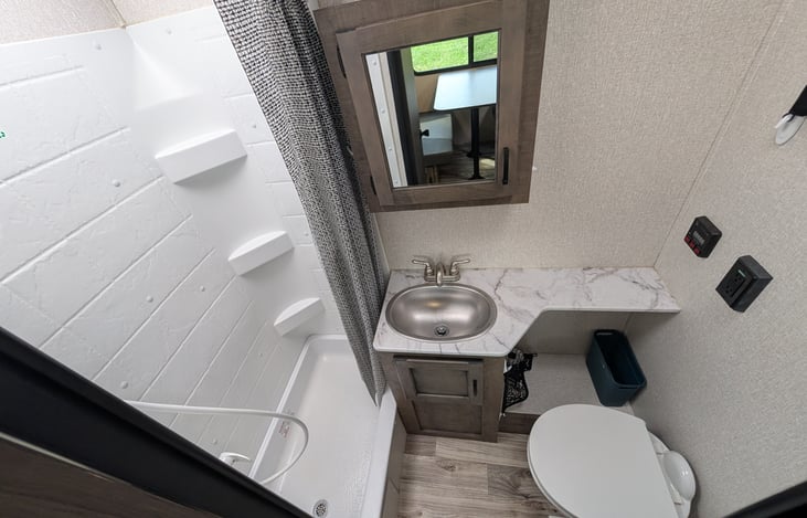 Full bathroom featuring a spacious walk-in shower with a overhead skylight for extra headroom, porcelain foot-flush toilet, vanity sink, and mirror with medicine cabinet storage.