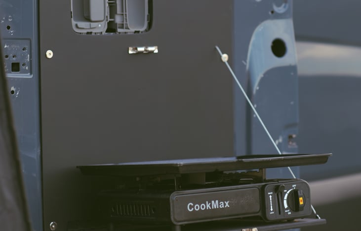 The van includes an induction cooker with an extra gas can, as well as a modern red electric stove for added cooking convenience.