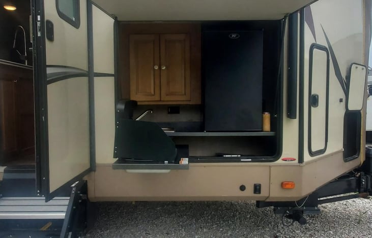 Outdoor kitchen including a stove, mini fridge, sink, and storage cabinet.