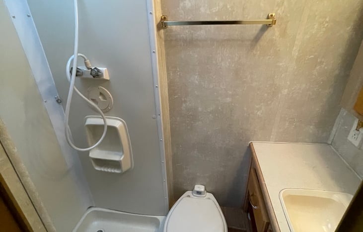 The fully equipped bathroom has shower, toilet, and sink all within  reach.