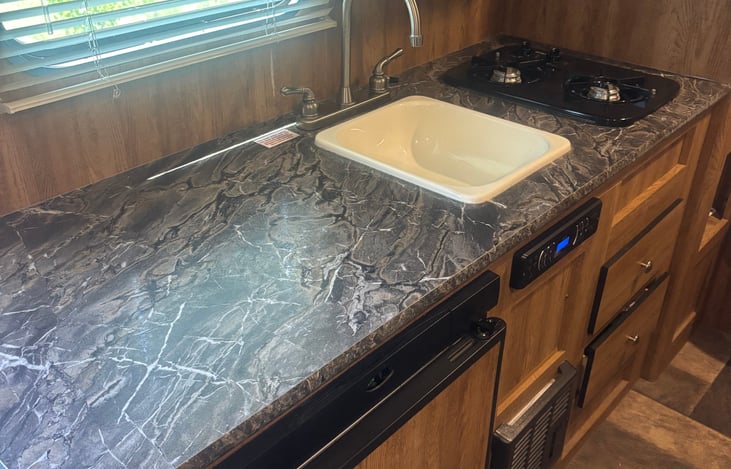 Cozy and Functional Kitchenette – Featuring a sleek marble-look countertop, dual-burner gas stove,  sink, mini fridge, and plenty of storage space. Everything you need to cook meals on the go