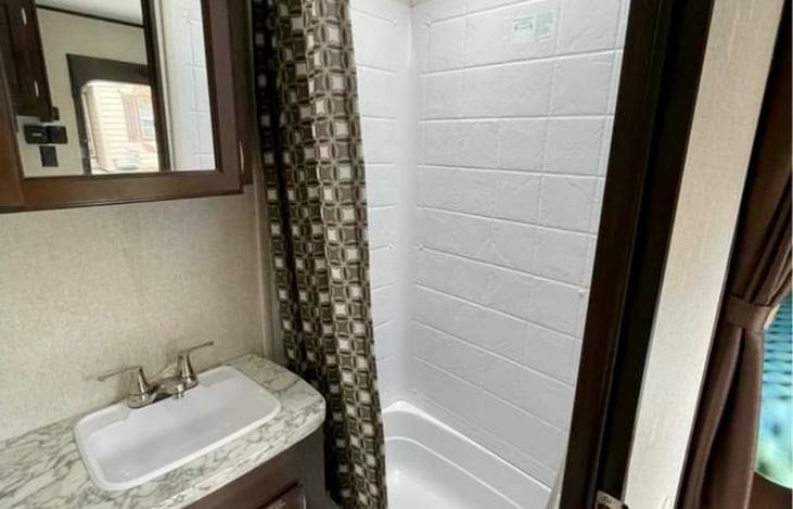 Spacious bathroom with tall shower, vanity, mirror medicine cabinet and comfortable toilet.