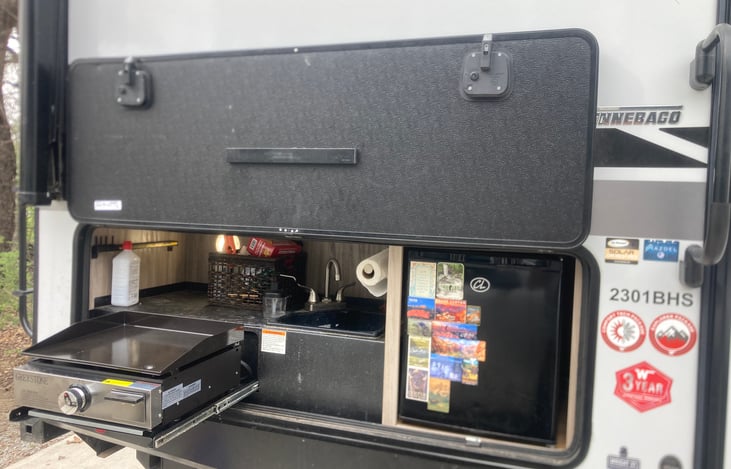 Outdoor Kitchen equipped with propane grill/ griddle, sink and mini fridge.