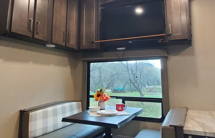Booth dining area with large window as well as overhead cabinets and a full size TV