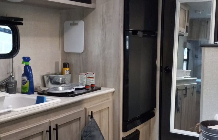 A Full-Functioning Kitchen with a sink, two-burner stove, mid-size fridge, microwave, and storage space for snacks and non-perishable food